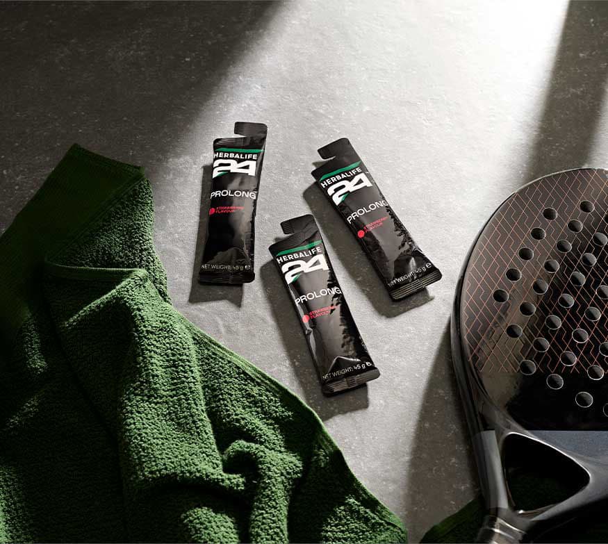 Tre bustine di H24 Prolong Energy Gel al gusto fragola appoggiate su una superficie grigia, accanto a un asciugamano verde e a una racchetta da padel.