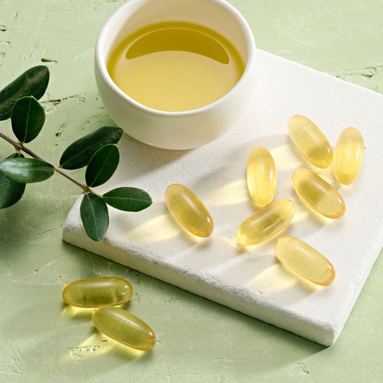 Le capsule di Herbalifeline Max su un piano chiaro, accanto a una ciotola di olio di pesce e a un ramoscello verde